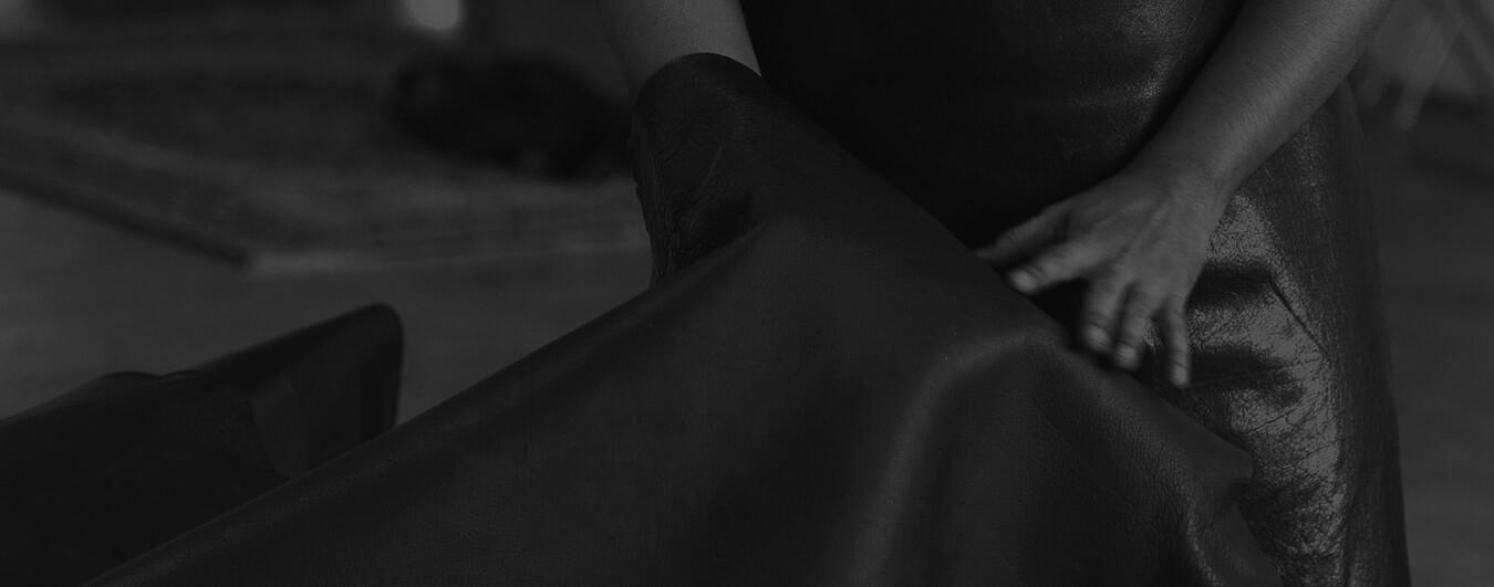A craftsman's hands grading a full-grain leather hide on the atelier floor